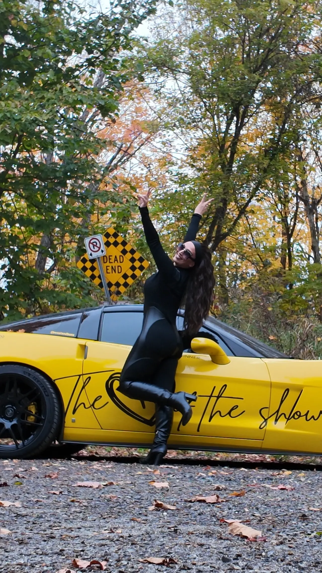 Chelsea mid-kick beside the Corvette, one arm raised to the sky.